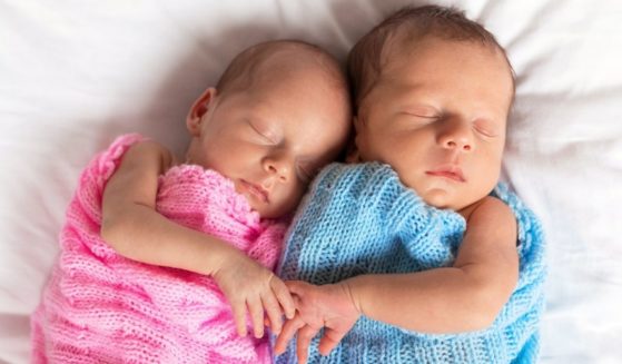 Newborn twins, a girl and a boy, cuddle together while sleeping.