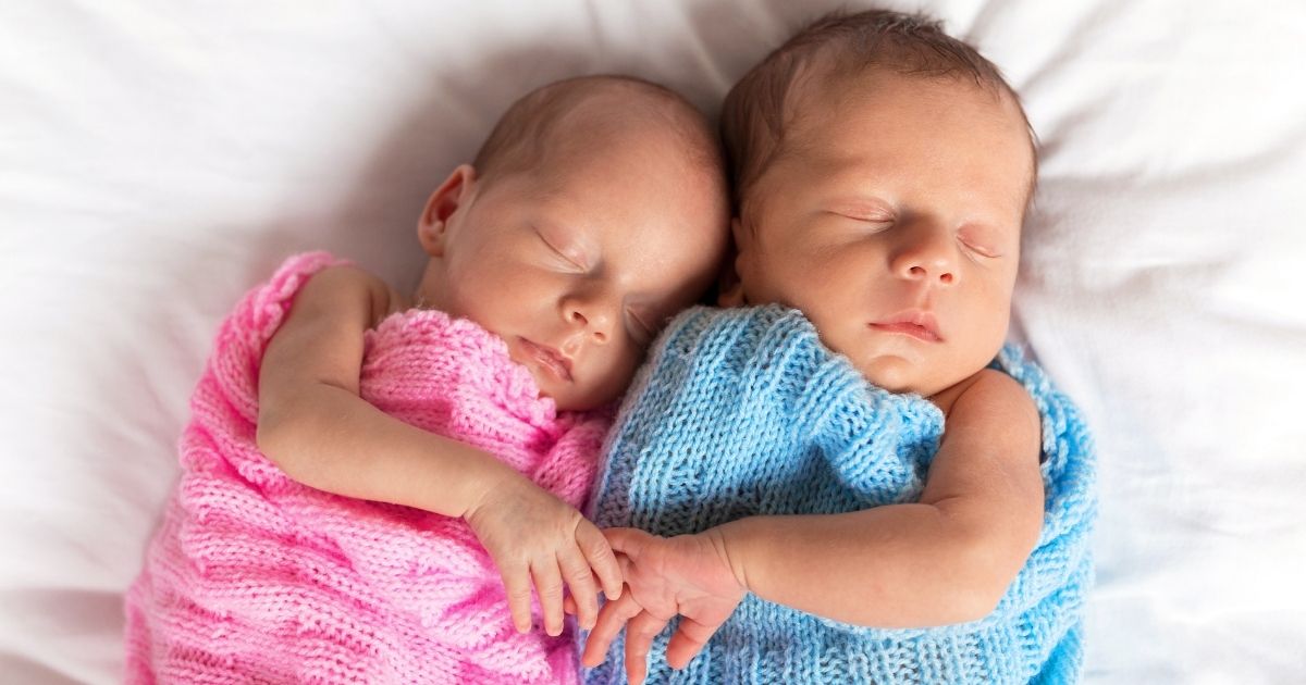 Newborn twins, a girl and a boy, cuddle together while sleeping.