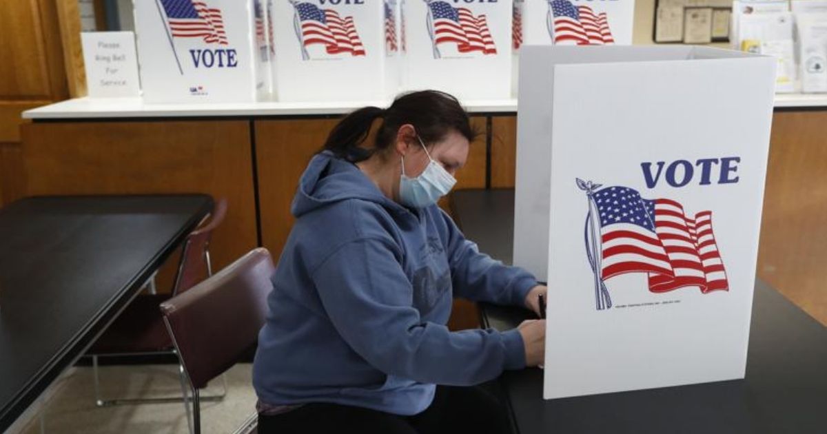 A woman wearing a mask is seen filling out an absentee ballot at City Hall in Garden City, Michigan.