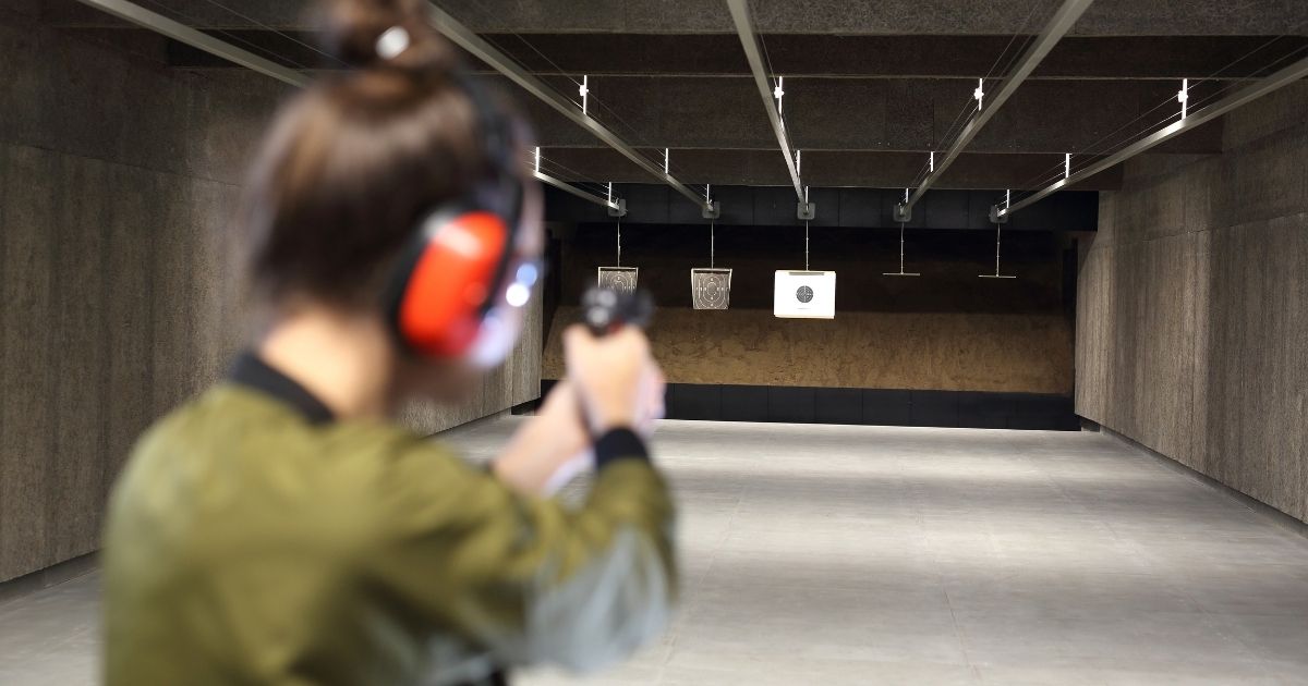 A woman shoots a handgun at a target at a gun range.