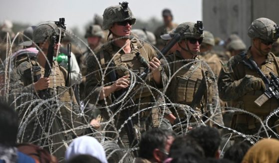 U.S. soldiers stand guard behind barbed wire as Afghans sit on a roadside near the military part of the airport in Kabul on Aug. 20, hoping to flee from the country after the Taliban's military takeover of Afghanistan.