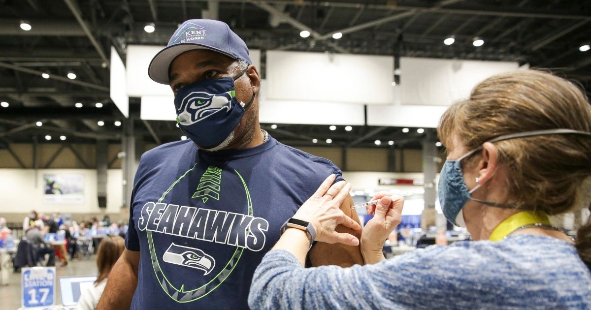 Cleveland Hughes wears Seahawks gear as he gets the Pfizer COVID-19 vaccine from Andrea Barnett at the Lumen Field Event Center in Seattle on March 13, 2021.