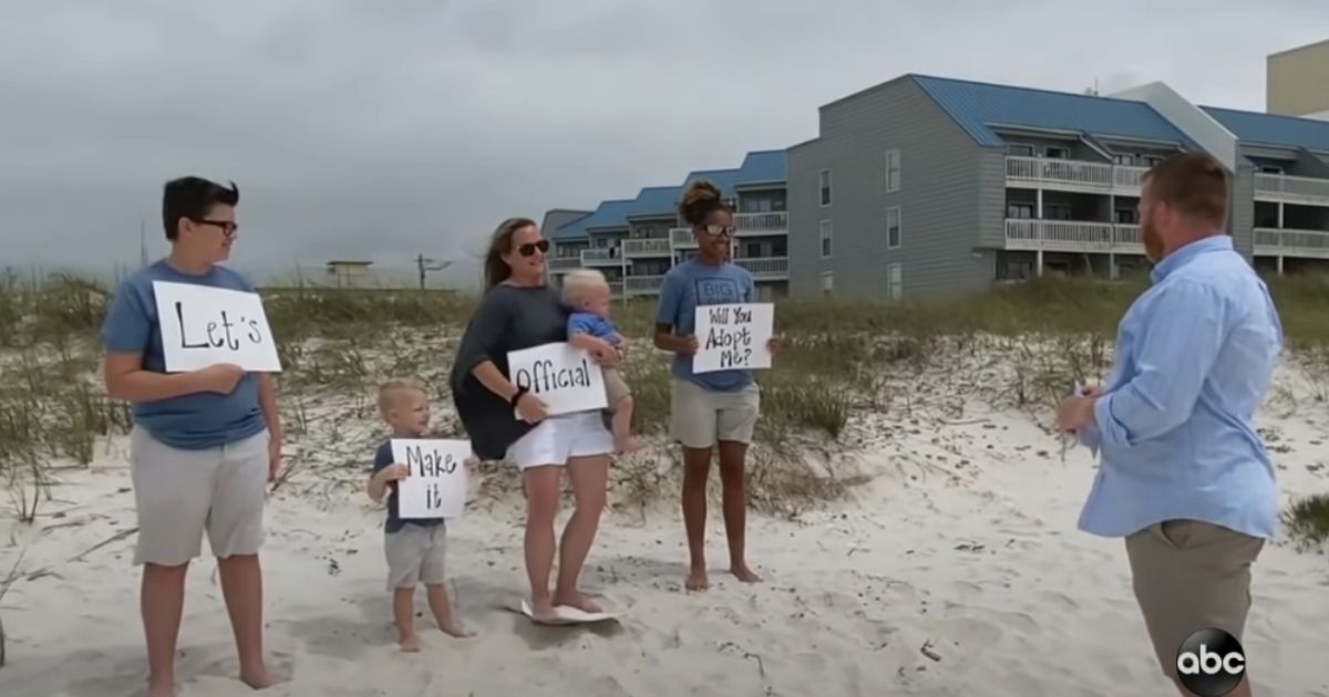 Alecia and her foster family hold up signs asking her foster dad, on his birthday, if he will adopt her.