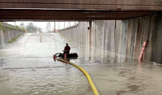 A driver sits on a truck in a flooded underpass being rescued by a firefighter.