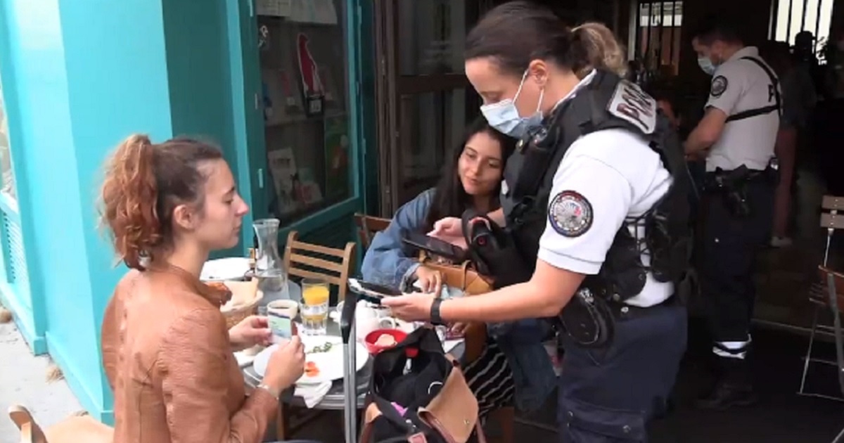 A Paris policewoman check's a diner's phone for proof that she'd received the coronavirus vaccine.