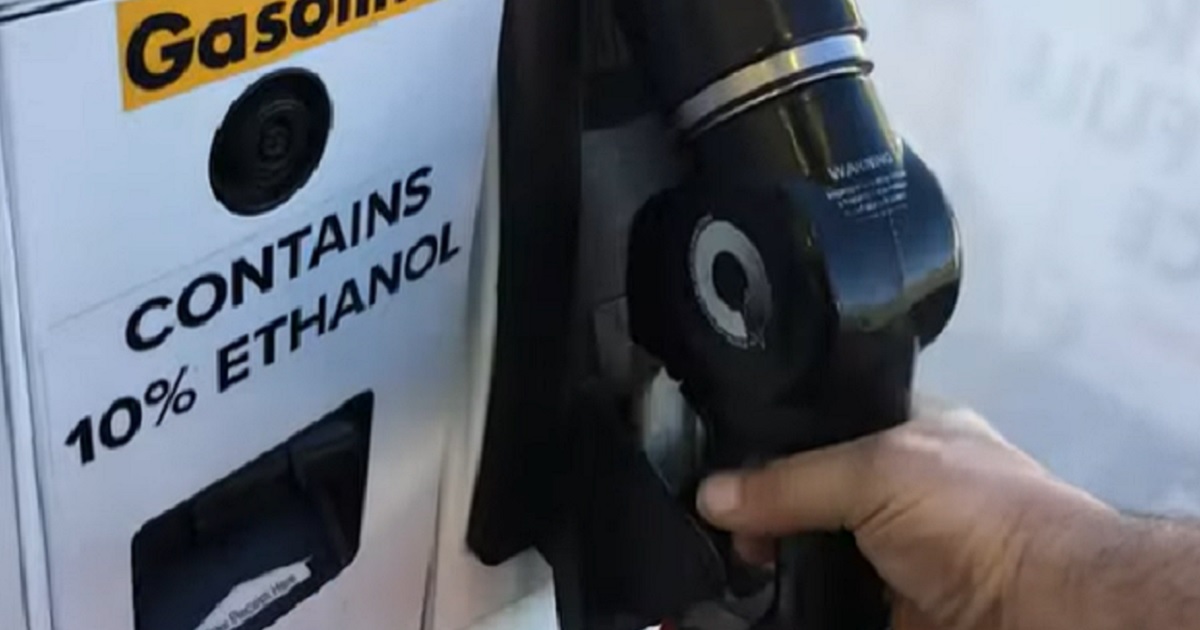 A hand hold a nozzle at a gas pump.