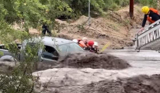 Floodwaters rage around a truck as rescuers extricate the passengers