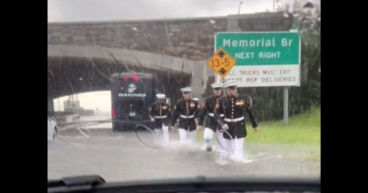 Marines in dress blues walk through floodwaters to help a stranded motorist.