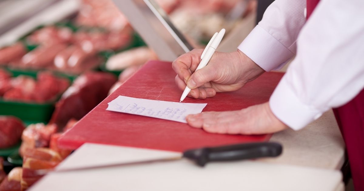 A butcher making notes at a meat counter.