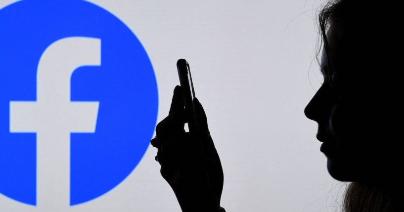 A woman can be seen looking at a smartphone while standing in front of the Facebook logo in Arlington, Virginia, on Aug. 17, 2021.