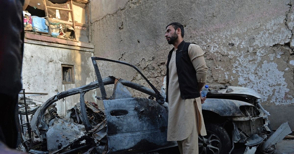 A brother of slain aid worker Ezmarai Ahmadi stands next to the wreckage of a vehicle that was damaged in the Aug. 29 American drone strike Afghanistan that killed Ahmadi, along with two other adults and seven children.