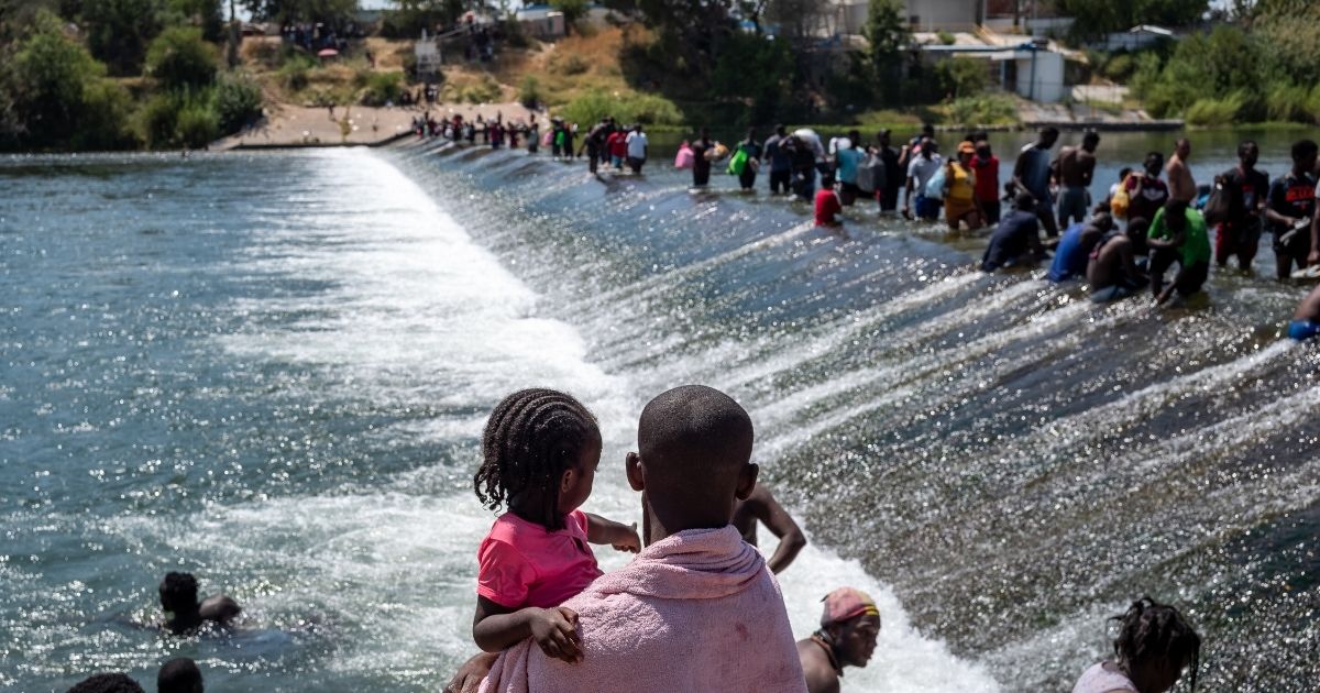 An illegal immigration from Haiti holds his daughter as others cross the Rio Grande.