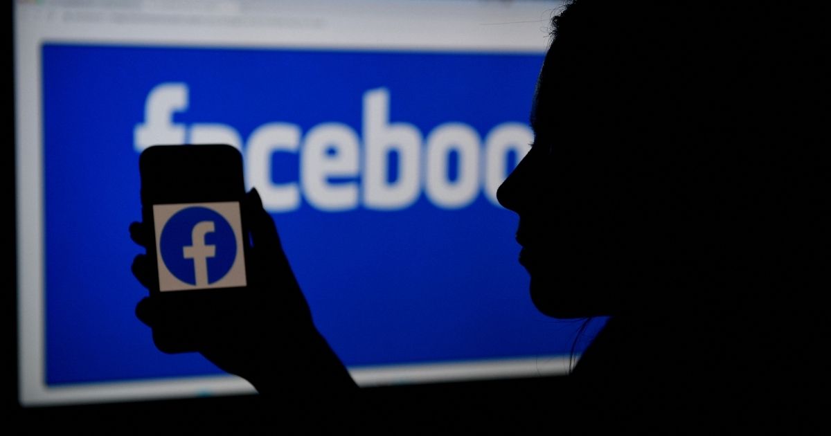 A photo shows a person holding up a smart phone with the Facebook logo standing in front of a screen showing the same logo in Arlington, Virginia, on April 7.