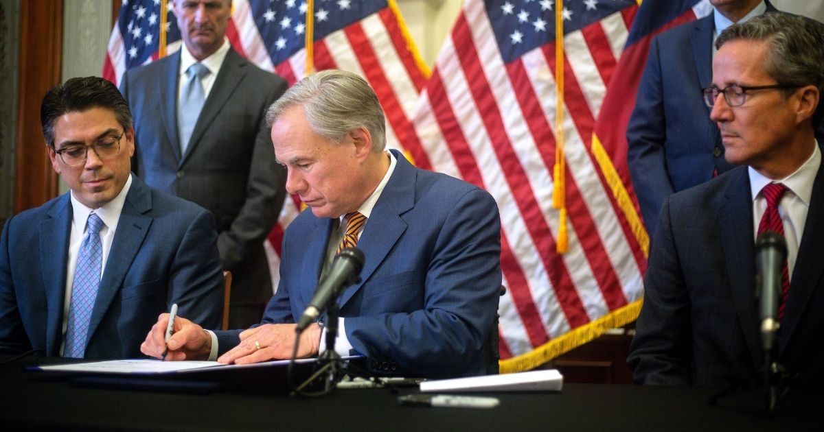 State Rep. Chris Paddie (L) and State Senator Kelly Hancock (R) watch as Texas Governor Greg Abbott signs Senate Bills 2 and 3 during a press conference at the Capitol on June 8, in Austin, Texas.