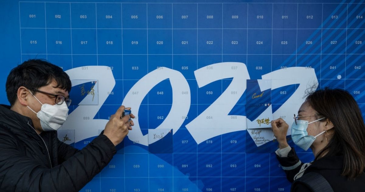 A man takes a photo of a woman as she signs a '2022' poster at an event held by the organizing committee of the Beijing 2022 Winter Olympics and Paralympics for international media at their headquarters at Shougang on April 12, in Beijing.