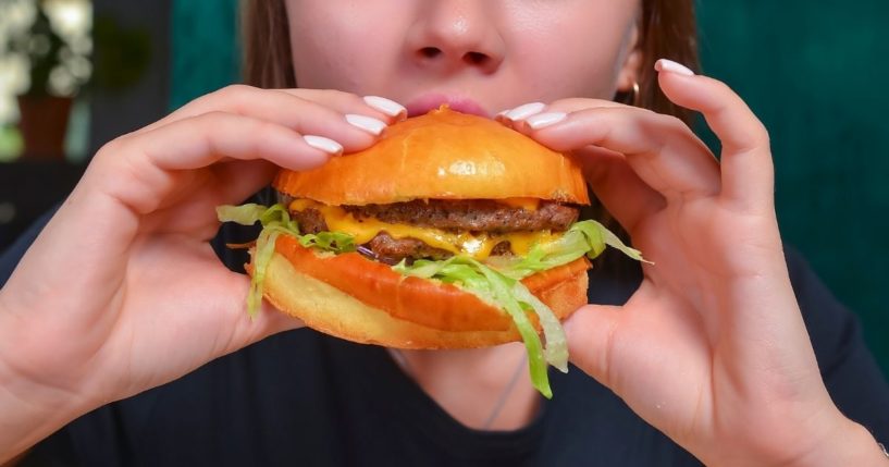 A woman eats a cheeseburger.