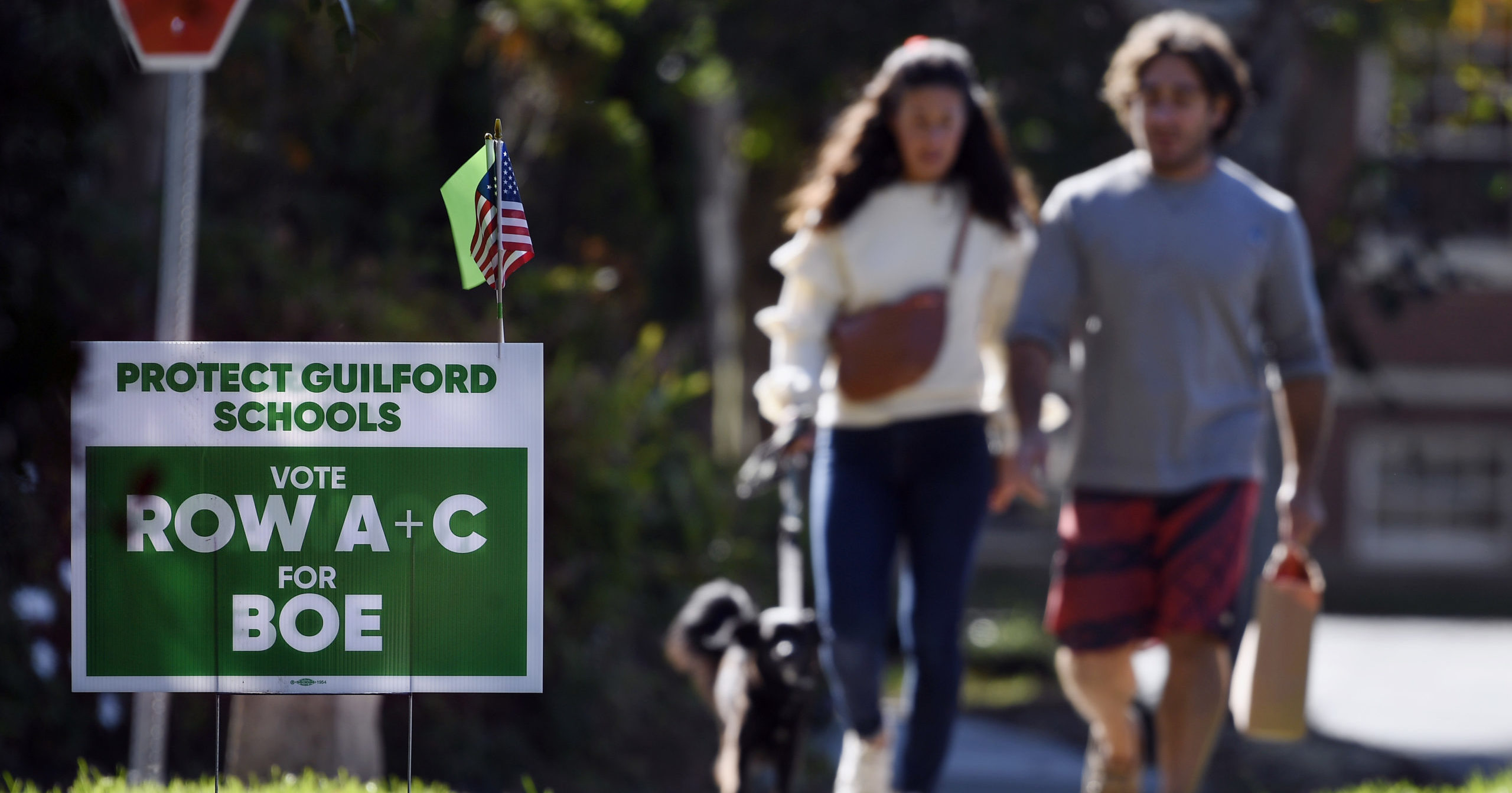 People walk near one of many signs around town centered around the upcoming Nov. 2 election in schools in Guilford, Connecticut on Tuesday.