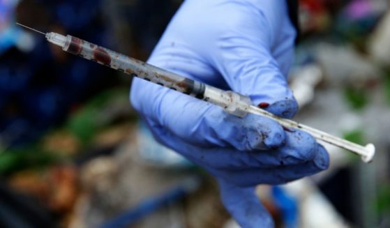 A volunteer worker holds up a used, blood-filled drug needle while cleaning up a homeless encampment in Everett, Washington on Nov. 8, 2017.