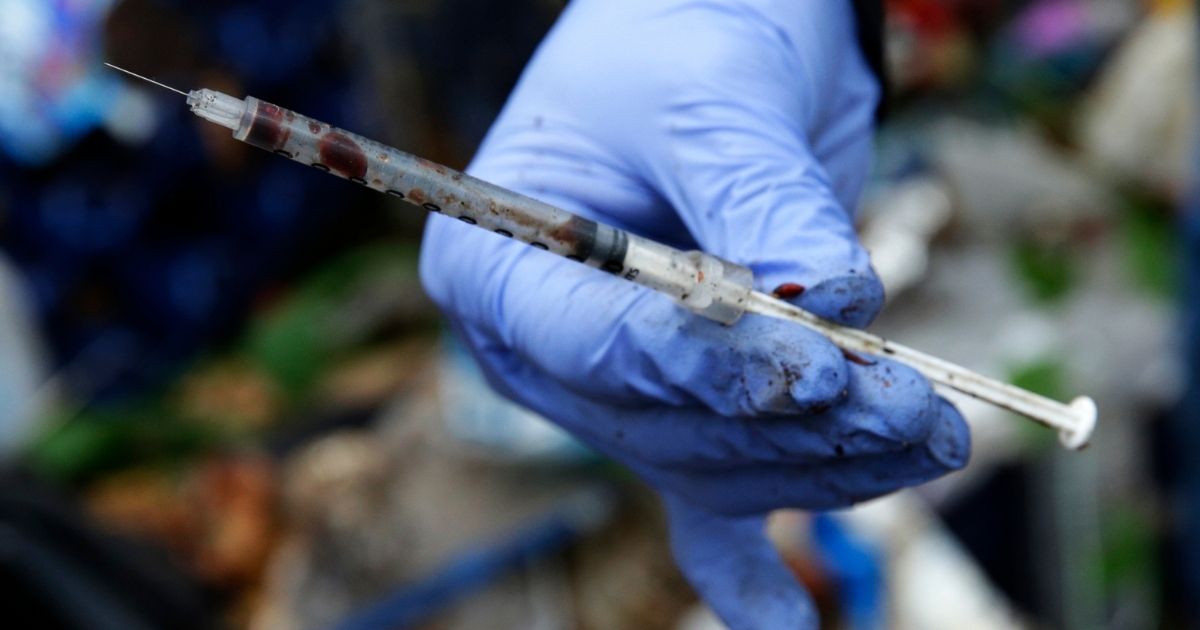 A volunteer worker holds up a used, blood-filled drug needle while cleaning up a homeless encampment in Everett, Washington on Nov. 8, 2017.