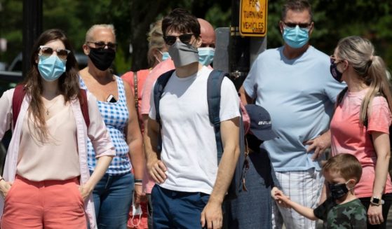 A group of people wearing masks stand on a street corner in Boston during July 2020.