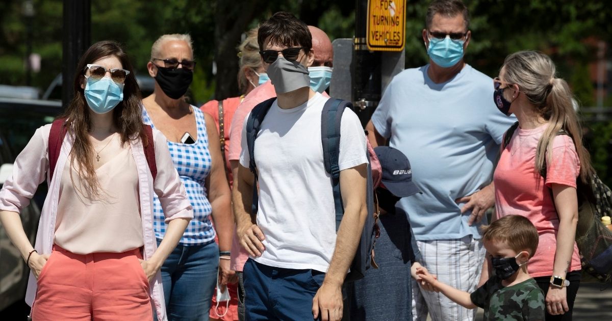 A group of people wearing masks stand on a street corner in Boston during July 2020.