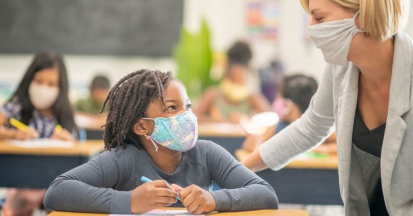 A masked teacher interacts with a masked student in this undated stock photo image. A Florida school district has come under fire for failing to advise parents of a special-needs student that they were tying a mask to the child's face every day.