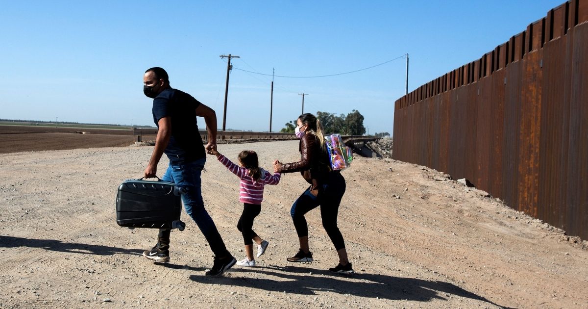 A family of migrants from Cuba runs across the border by the wall separating the United States and Mexico to turn themselves over to authorities on May 13, in Yuma, Arizona.