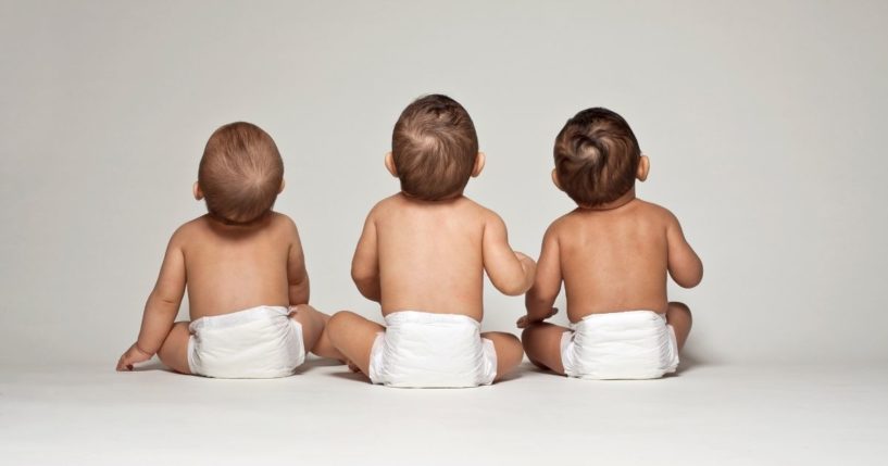 A stock photo shows three babies in diapers facing away from the camera.