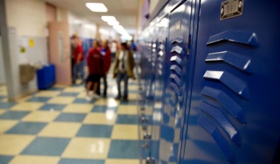 Stock photo of a high school hallway with a group of students at the far end.