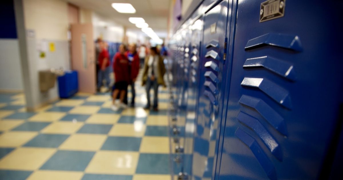 Stock photo of a high school hallway with a group of students at the far end.