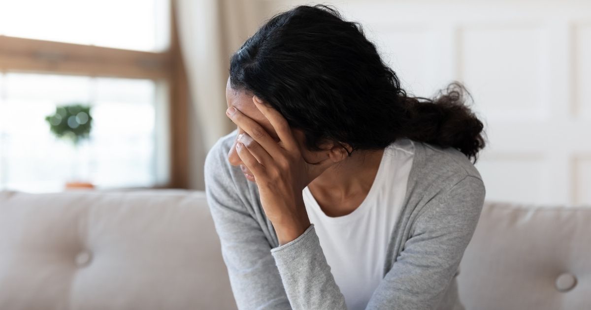 A stock photo shows a woman sitting with her face in her hand, looking sad.