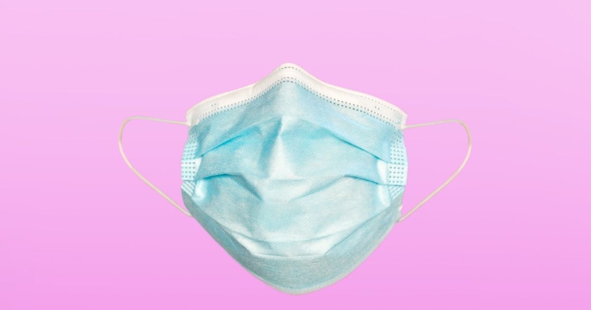 A stock photo shows a COVID-19 mask on a pink background.