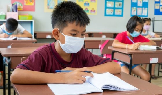 Elementary school students are seen wearing masks and sitting at their desks.