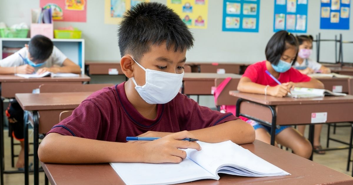 Elementary school students are seen wearing masks and sitting at their desks.