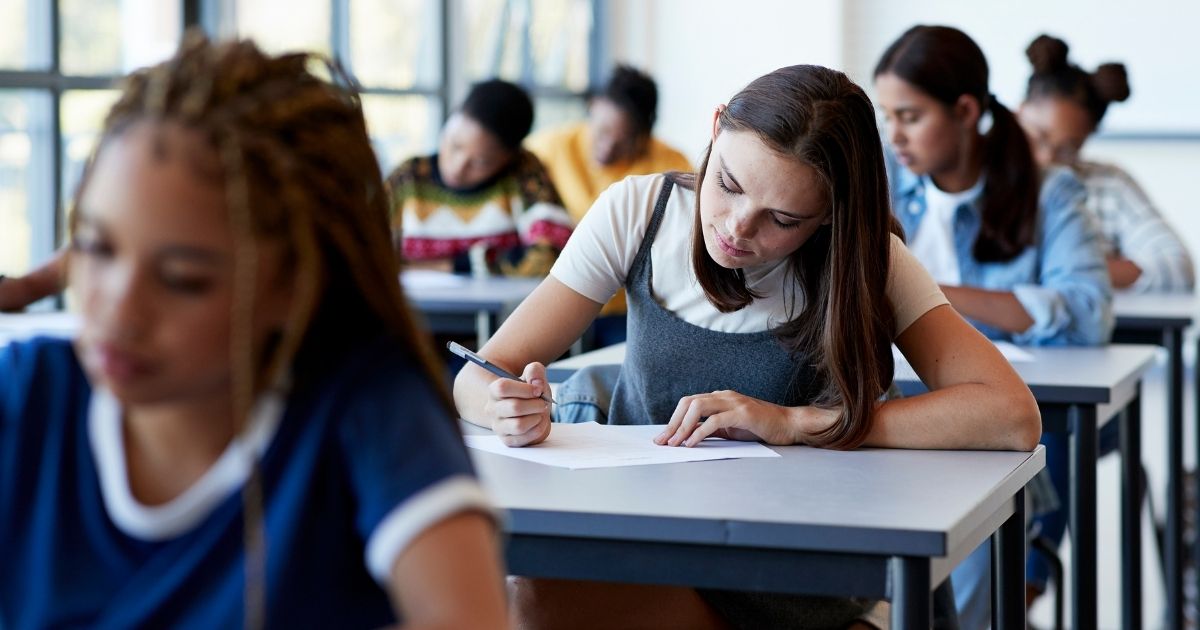 A stock photo shows students sitting in class and writing at their desks.