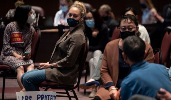 A woman with a sign sits with other people at a Loudoun County Public Schools board meeting in Ashburn, Virginia, on Oct. 12.