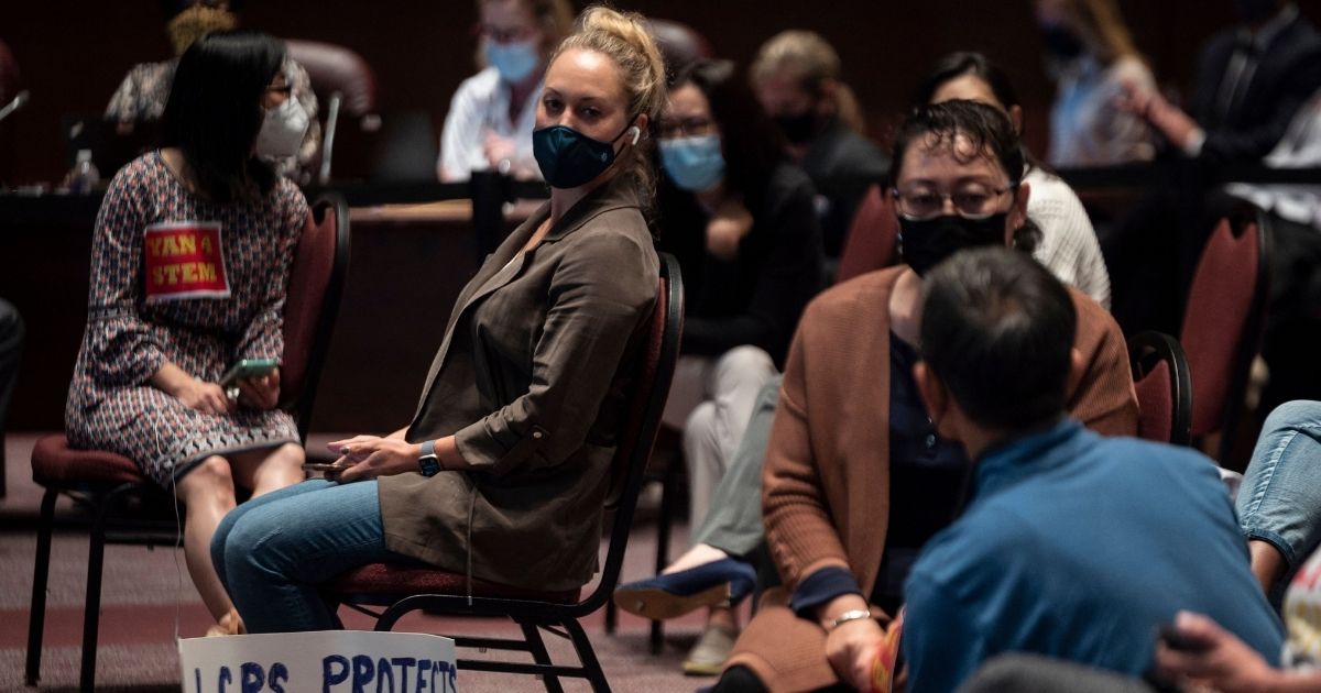 A woman with a sign sits with other people at a Loudoun County Public Schools board meeting in Ashburn, Virginia, on Oct. 12.