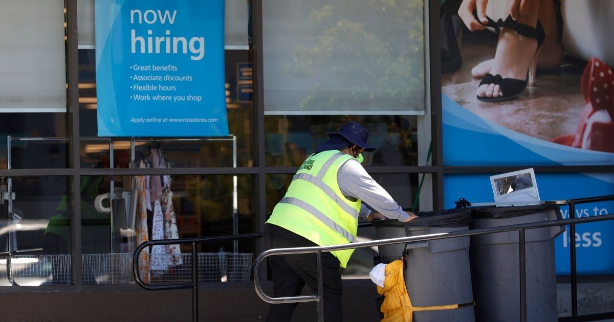 A worker pushes a cart past a "Now Hiring" sign outside of a Ross store in Sausalito, California, on June 3.