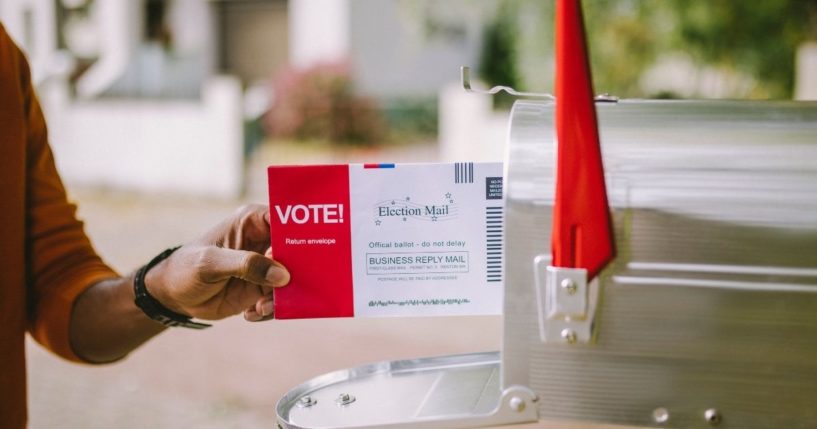 A man puts an absentee ballot in a mailbox in the above stock image.
