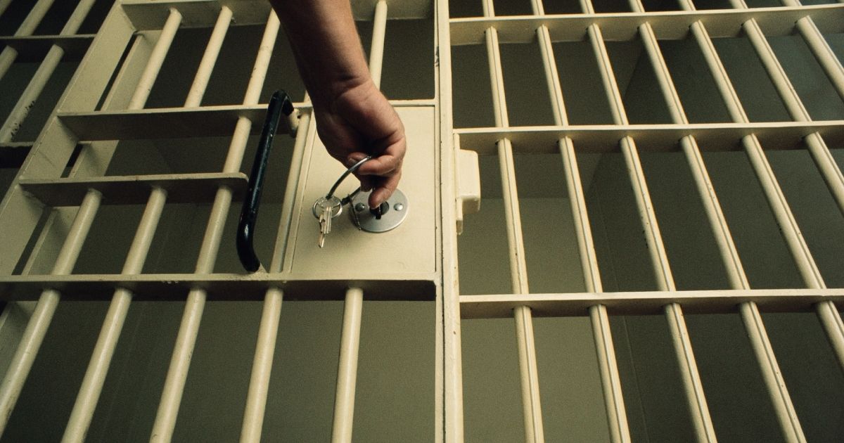 A man locks a prison cell door in the above stock image.