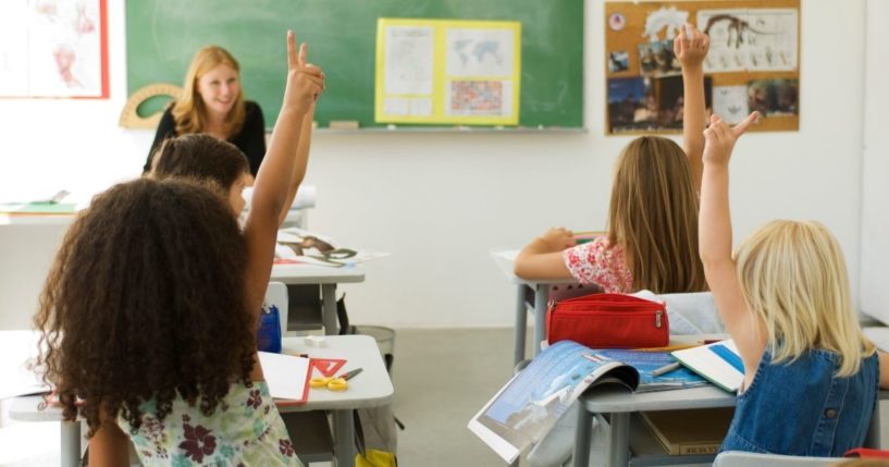 Children raise their hands in a classroom in this stock image.