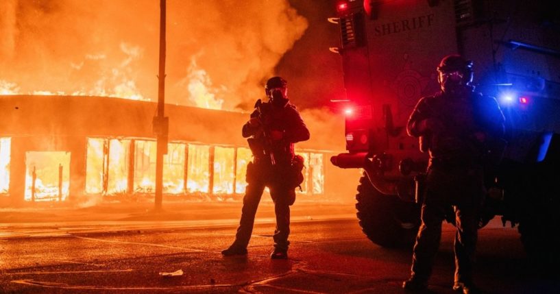 Police patrol an intersection next to a burning building during rioting in Kenosha, Wisconsin, on Aug. 24, 2020.