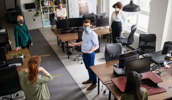 Office workers wearing face masks stand far apart from one another in an office