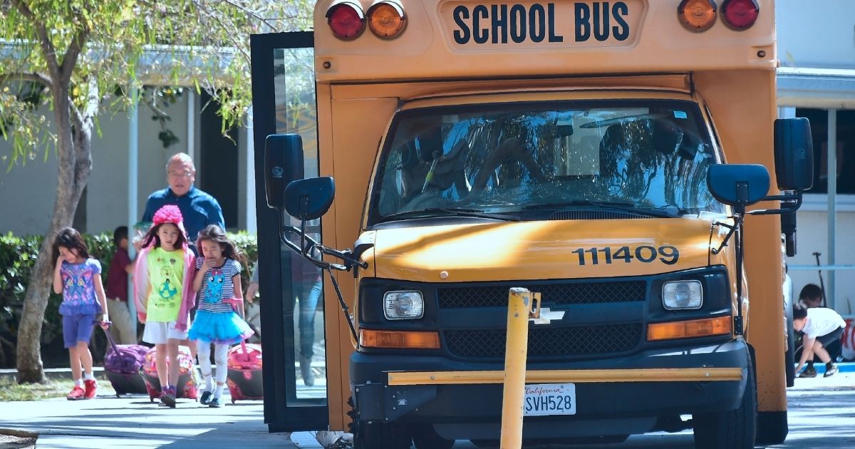 Children walk past a school bus in Monterey Park, California, in this file photo from April 2017. More than two-thirds of America's 500 largest school districts still require students to wear masks, while at least 14 other countries have halted the practice.