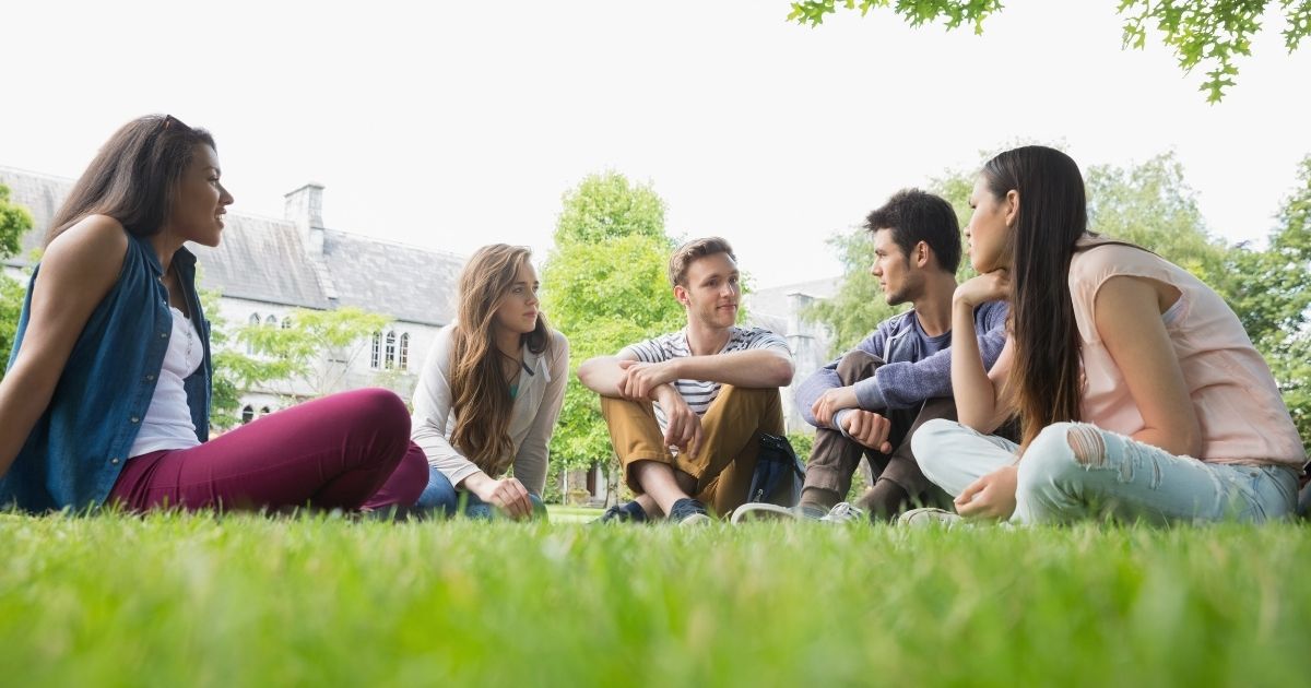 Students sit outside in the grass at a university campus.