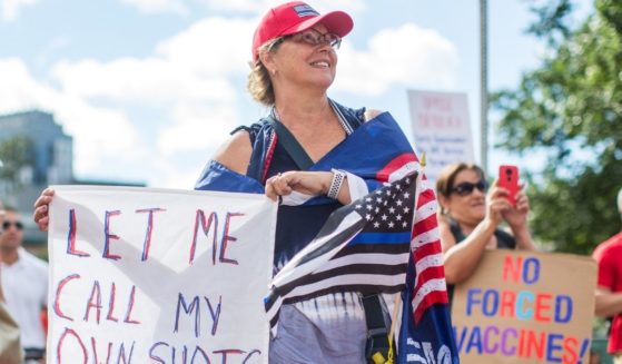 Anti-vaccine activists hold signs in front of the Massachusetts State House during a protest against Gov. Charlie Baker's mandate that all Massachusetts school students enrolled in child care, pre-school, K-12, and post-secondary institutions must receive the flu vaccine this year on Aug. 30, 2020, in Boston, Massachusetts.