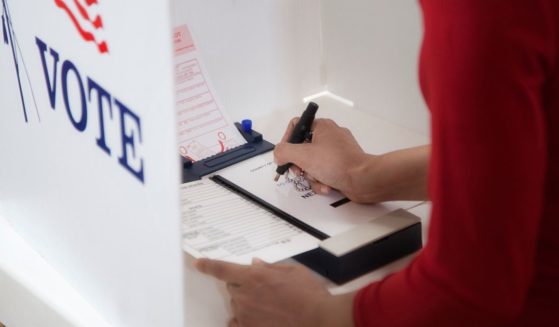 A stock photo shows an individual voting at a polling place.