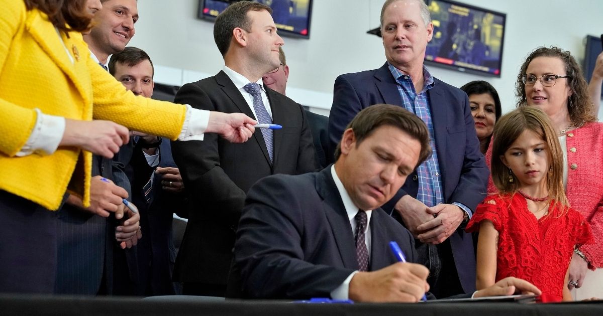 Florida Gov. Ron DeSantis, seated, signs a bill in front of supporters and members of the media during a news conference on Nov. 18, 2021, in Brandon, Florida. The bill is among four signed Thursday that protect Florida residents from coronavirus vaccine and mask mandates.
