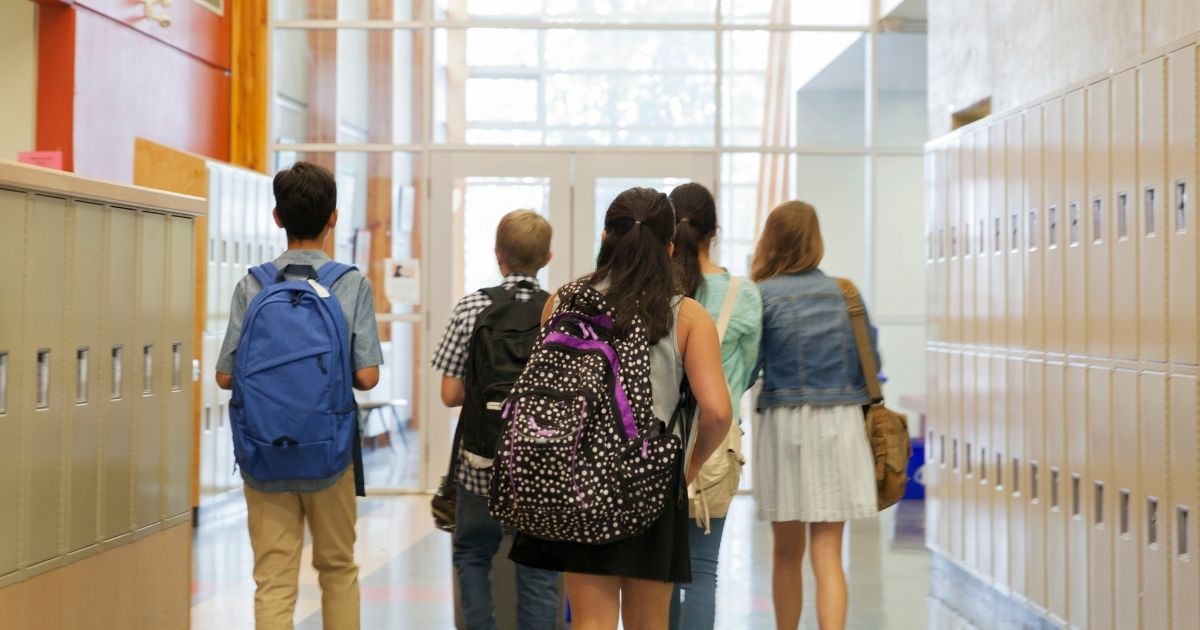 Children wearing backpacks walk down a hallway in this stock image.