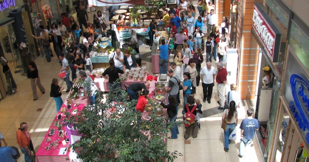 This photo shows a mall full of people looking into stores, shopping, and getting food.